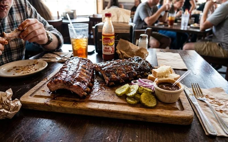 A wooden serving board with a rack of baby back ribs on one side and a rack of spare ribs on the other, showing the size and shape difference between the two cuts