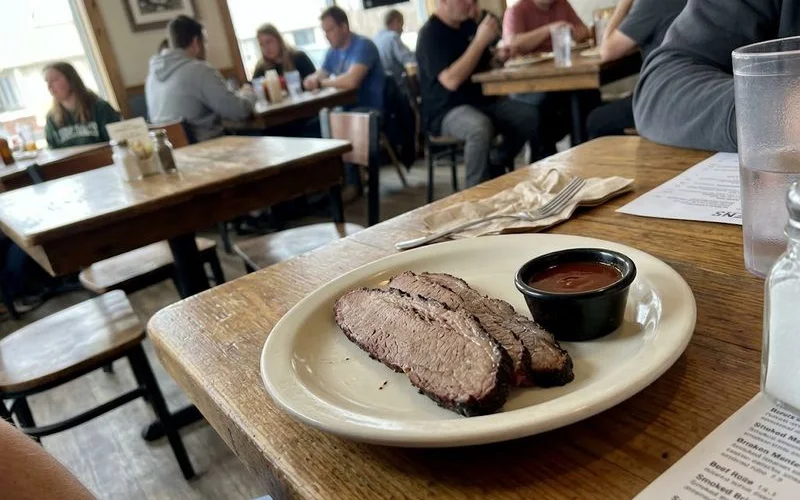 A BBQ plate arranged to highlight dietary-friendly choices, with plain smoked brisket, a side of vegetables, and sauce served separately in a small dish